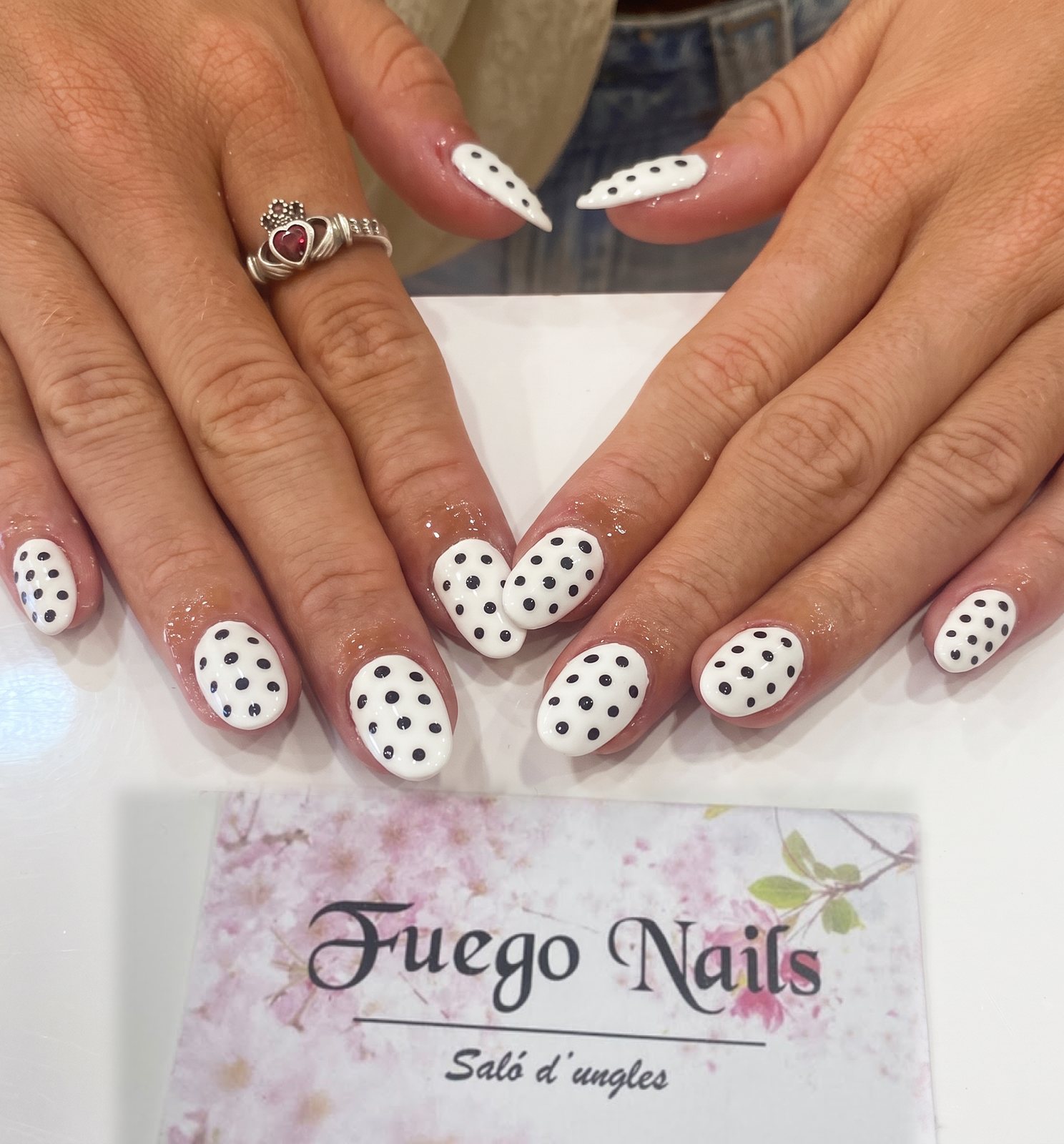Uñas decoradas con lunares blancos, sujetando una tarjeta de Fuego Nails.