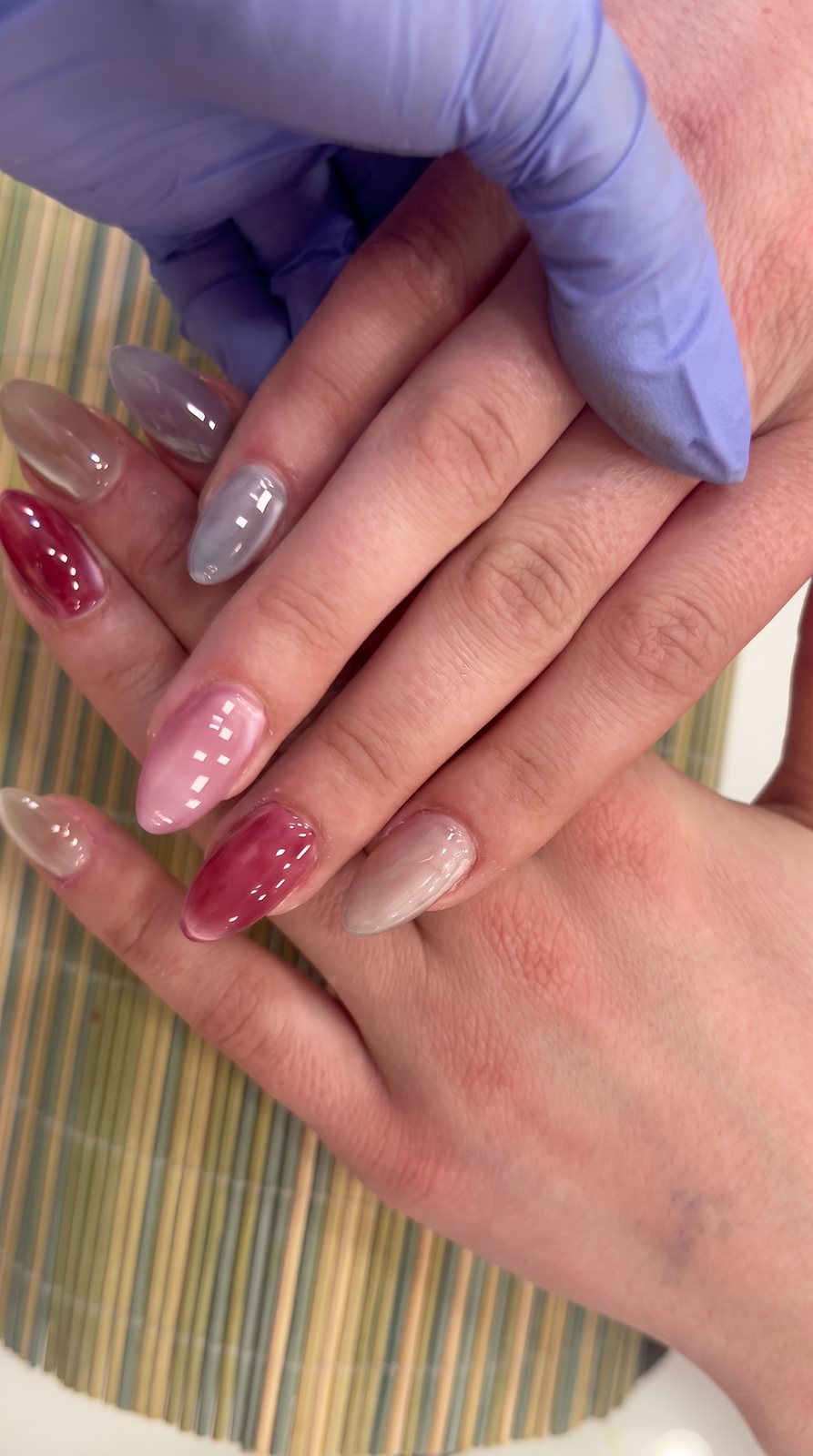Mano con guante aplicando esmalte a una clienta con uñas en burdeos y gris.